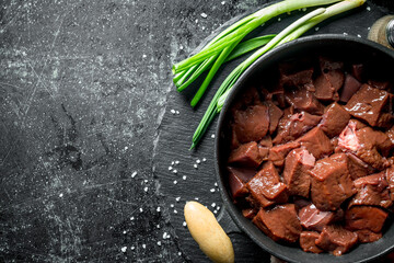 Poster - Pieces of raw liver in a saucepan with green onions.