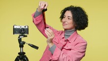 Portrait Of Creative Photographer In Photo Studio. Developing Analog Camera Film. Smiling Mature Female Photographer Holding Reviewing Film Negatives In Studio Background With Vintage Camera On Tripod