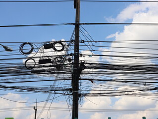 Many wires are messy with power line cables on the concrete pole against the blue sky