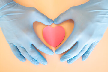 Male hands in blue medical gloves hold a pink heart symbol. Hands holding a pink heart.The gesture symbolizes of love. Help and volunteering, Insurance health care, pink love, Valentine day concept.