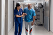 © wavebreak3 - Diverse female doctor helping senior male patient walk in corridor, copy space