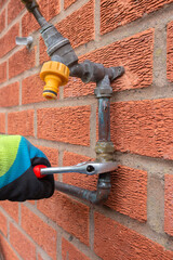 Wall Mural - Man replacing burst copper water pipe outdoors. Unscrewing a brass connector with a spanner wrench