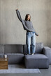 © F8  \ Suport Ukraine - Positive young woman in wireless headphones and casual clothes listening to music with pleasure and dancing of sofa in light modern living room