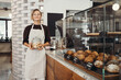 Young female baker entrepreneur standing at the counter of bakery and coffee shop.
