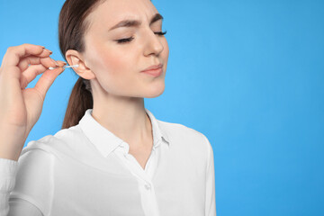 Wall Mural - Young woman cleaning ear with cotton swab on light blue background, closeup. Space for text