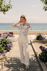 Wall Mural - Nice young Caucasian girl is standing in garden enjoying summer day. Brunette wears casual clothes posing near beach. Relaxing time concept.