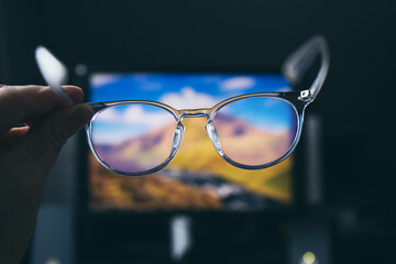 Selective focus on transparent clear blue light computer glasses and computer screen glowing on the background in home or office. Blue light glasses protect eyes and eyesight from screens blue light.