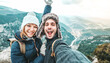 © Davide Angelini - Happy couple of hikers taking selfie picture on top of the mountain - Two travelers with backpack smiling together at camera - Travel blogger influencer streaming using smart mobile phone device
