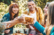 © Davide Angelini - Happy friends cheering beer glasses in brewery pub garden - Group of happy people enjoying happy hour time sitting at bar table - Beverage, lifestyle and friendship concept