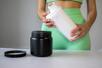 An athletic woman holds a prepared protein suplements or electrolytes for sport in a shaker bottle.