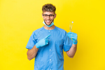 Wall Mural - Dentist blonde man holding tools isolated on background pointing to the side to present a product