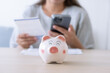 © StockerThings - Woman pay household expenses using mobile phone and save money in piggy bank