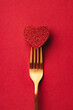 Valentine's day greeting card in minimal style with shiny heart pierced by golden fork on red background.