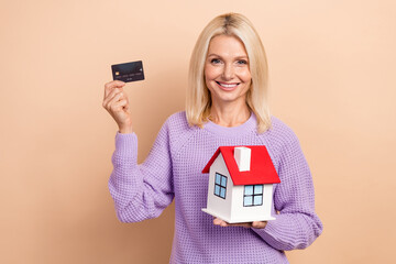 Poster - Photo of charming cheerful lady hands hold show debit card little house isolated on beige color background