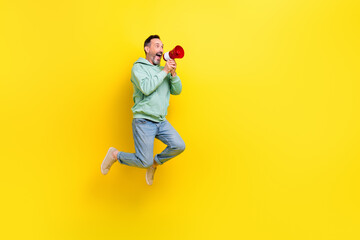 Poster - Full length photo of cool excited man wear green sweatshirt telling toa announcement empty space jumping high isolated yellow color background