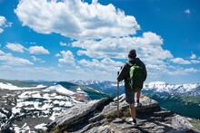Man Standing On Top Of The Mountain Looking At Beautiful View. Early Summer Landscape With Green Meadows And Snow Covered Mountains.  Trail Ridge Road. Rocky Mountains National Park, Colorado, USA.