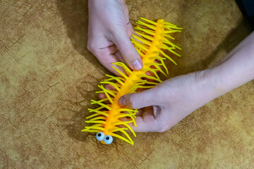 A closeup photo of a bright yellow rubber toy with rubbery hairs and legs, that resembles a caterpillar with a funny drawn on face, being held in a male hand