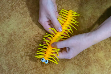 A closeup photo of a bright yellow rubber toy with rubbery hairs and legs, that resembles a caterpillar with a funny drawn on face, being held in a male hand