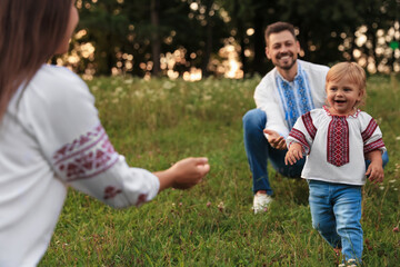 Canvas Print - Happy parents in embroidered Ukrainian shirts playing with their cute daughter outdoors