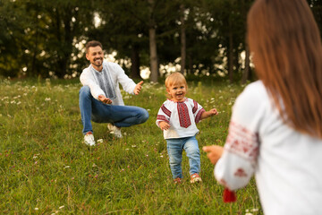 Canvas Print - Happy parents in embroidered Ukrainian shirts playing with their cute daughter outdoors