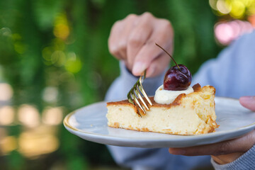 Wall Mural - Closeup image of a woman holding and eating cheesecake with fork