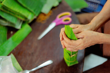 Focus old woman with traditional Vietnamese dress (ao ba ba) Making (wrapping) Tet Cake, the Vietnamese lunar new year Tet food outdoor by hands.