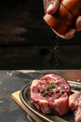 Wall Mural - chef pours pepper on raw steak. Backstage of preparing grilled pork meat. Culinary, cooking concept. place for text