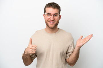 Poster - Young caucasian man isolated on white background holding copyspace imaginary on the palm to insert an ad and with thumbs up