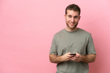 Wall Mural - Young caucasian man isolated on pink background sending a message with the mobile