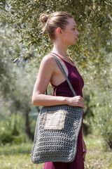 Wall Mural - Young woman wearing red summer dress and carrying big green crochet bag in the olive tree plantation, summer fashion style, relaxed vacation in nature