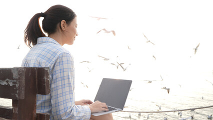 Beautiful white woman typing on a laptop at the pier. Freelance work, Anywhere work, 5G Technology.