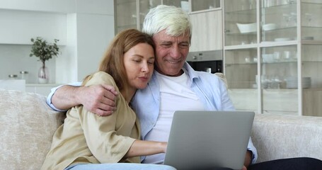 Wall Mural - Adult daughter woman teaching senior dad to use online app on laptop computer, speaking, telling, explaining Internet application work, pointing at display, laughing, showing funny media content