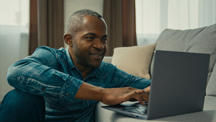 African american middle aged businessman typing laptop mature ethnic male programmer freelancer work remote home in cozy living room smiling man writing email using computer app chatting on internet