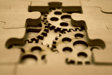 wooden gears under the puzzle, the concept of moving to the next level. Cog wheels coming out from underneath a jigsaw puzzle. solving the problem concept - puzzles and cogwheels