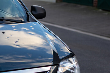 Black car engine hood with many hail damage dents show the forces of nature and the importance of car insurance and replacement value insurance against hail dents of storm hazards extreme weather