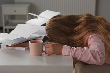 Wall Mural - Young tired woman sleeping near books at white table indoors