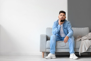 Wall Mural - Stressed young man sitting on sofa at home