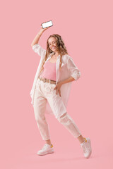 Wall Mural - Young woman in earphones with mobile phone dancing on pink background