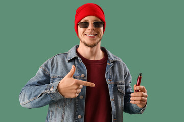 Wall Mural - Stylish young man with disposable electronic cigarette on green background