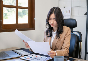 Young businesswoman sitting at workplace and reading paper in office