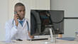 © stockbakers - African Doctor Talking on Phone while Working on Laptop