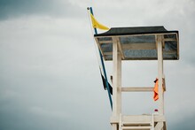 Empty White Lifeguard Tower With A Yellow Flag On The Beach In Windy Weather. Beach Lifeguard Tower With Yellow Flag Indicator. Nobody. Holiday Recreation Concept.