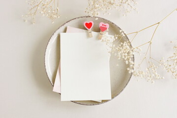 Wall Mural - Valentines Day blank papers, greeting cards mockup with clothespins hearts on a plate  and flowers top view  on beige background.