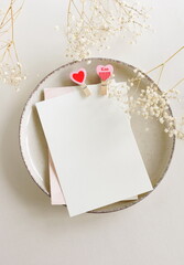 Wall Mural - Valentines Day blank papers, greeting cards mockup with clothespins hearts on a plate  and flowers top view  on beige background.