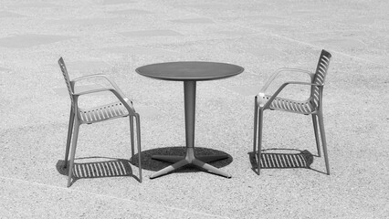 Black and white photo of two chairs at an empty table, selective focus.