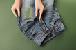 Woman holding jeans with stain on green background, top view