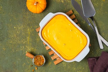 Canvas Print - Cottage cheese casserole with pumpkin and raisins in a rectangular baking dish on a green concrete background.