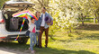 © Angelov - Happy family standing together near a car with open trunk enjoying view of rural landscape nature. Parents and their kid leaning on vehicle luggage compartment. Weekend travel and holidays concept.