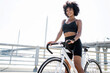 © muse studio - Smiling young woman curly-haired contented activity bike riding in a tracksuit.