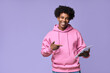 © insta_photos - Happy cool African American teenage guy teen boy model wearing pink hoodie holding tab using digital tablet pointing at device advertising online learning isolated on light purple background.